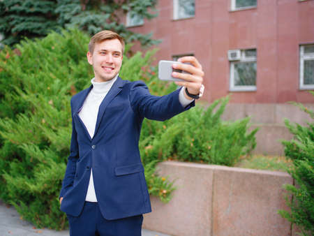 Young businessman in a suit outdoors with phone in hands.の写真素材