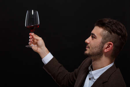 The fashionable guy lifted a glass of wine and examined it on a black backgroundの写真素材