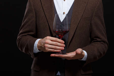 Fashionable man holding a glass of wine palm on a black backgroundの写真素材