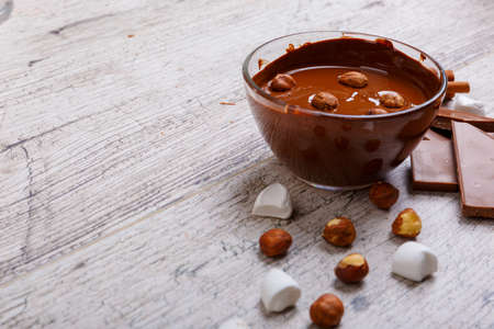 Bowl of melted milk chocolate with hazelnuts on the tableの写真素材