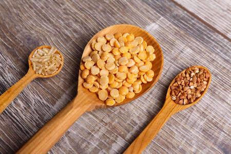 Three different sized wooden spoons are filled with cereals on the tableの写真素材