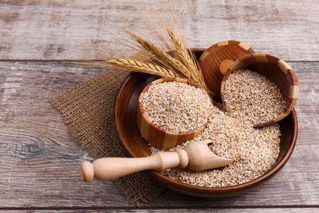 Wheat groats in a wooden plate with two potsの写真素材