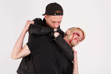 A beaten up guy with blood and bruises on his face is strangled by a guy. Isolation.の写真素材