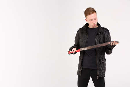 A boy in black clothes stands and looks at the machete. Isolation.の写真素材
