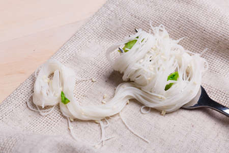 Rice noodles with greens are wound on a fork. Indoors. Close-up.