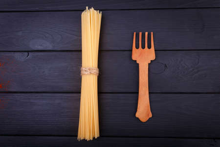 On a table is a bunch of spaghetti and a wooden fork. View from above. Indoors.の写真素材