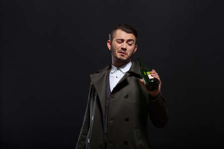 A man on a black background holds a bottle in his hand, looks into the bottle, behind the ear a cigarette.の写真素材