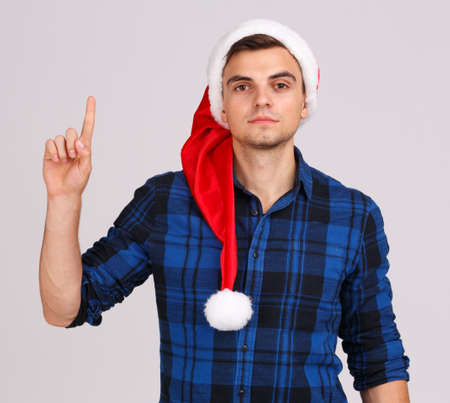 A young man in Santas hat points with his finger up.の写真素材