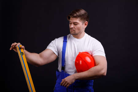 An employee with a spirit level in his hand holds it vertically on a black backgroundの写真素材