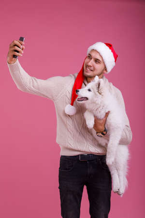 The guy makes selfie with his samoyed and looking both into the camera on a pink backgroundの写真素材