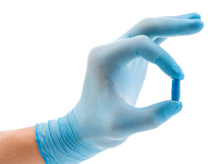 A hand in a blue glove holds a blue capsule, isolated on a white background