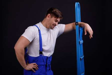 The worker leaned on the stepladder with one hand on a black backgroundの写真素材