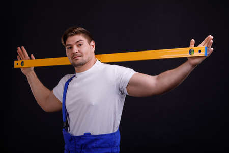 Worker holds a spirit level behind the neck on a black backgroundの写真素材
