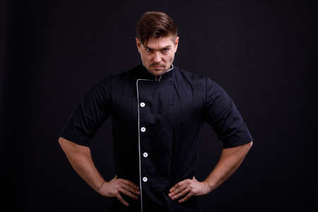 A man in a black tunic holds his hands in the sides on a black backgroundの写真素材