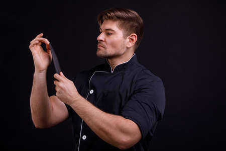 The man checks the sharpness of the knife blade with the second hand on a black backgroundの写真素材