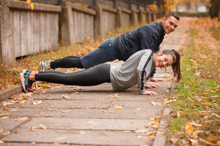 A sporty couple are squeezed from the ground. Outdoors in the autumn park.の写真素材