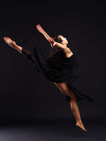 A girl dancer makes a leap in the twine. On a black background.の写真素材