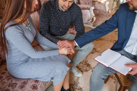 A couple at a reception at a psychologist hold their hands together and the doctor put his hand on topの写真素材
