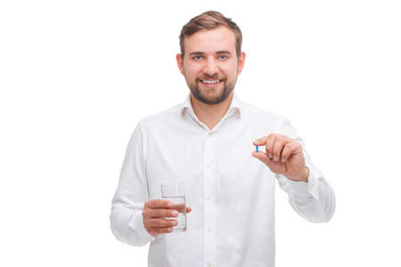 A guy is holding a glass of water and a capsule in his hand on a white isolated backgroundの写真素材