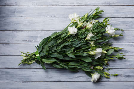 A bouquet of white Japanese roses tied up with a green ribbon close-up on a gray wooden background