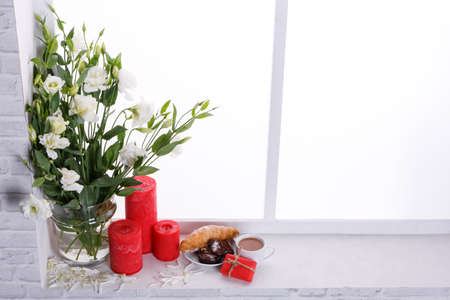 Japanese white roses in a vase with feathered petals next to candles, a croissant in a plate with a...