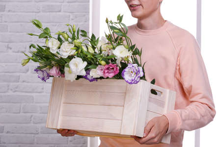 A guy in a beige sweater holds a wooden box with Japanese different roses from belowの写真素材