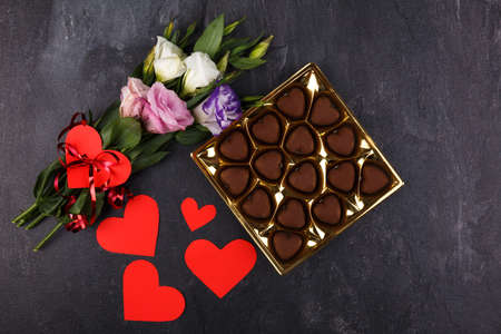 A bouquet of Japanese roses tied with a ribbon and a box of chocolates and carved hearts on a stone background. View from aboveの写真素材