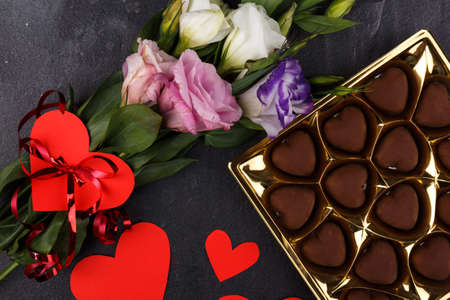 A bouquet of Japanese roses and a box of chocolates is not completely shown with carved hearts on a stone background. The view from above is close upの写真素材