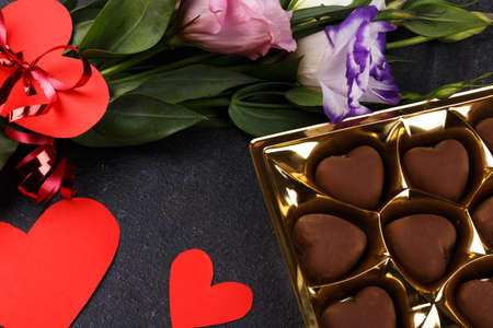 A bouquet of Japanese roses bandaged with a ribbon with a heart with a box of chocolates. Carved hearts are shown not completely on a stone backgroundの写真素材