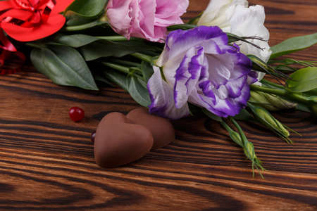 A bouquet of Japanese roses lie next to candy in the form of a heart and cranberries on a wooden backgroundの写真素材