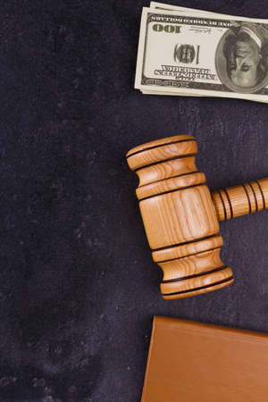 A brown notepad, a wooden judge hammer and a bundle of dollars money lie on a stone background. View...