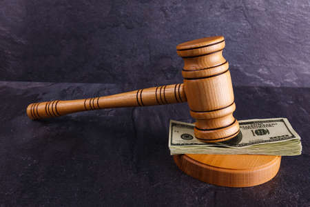 A bundle of dollars is stacked exactly between the wooden hammer of the judge and the stand on a stone backgroundの写真素材