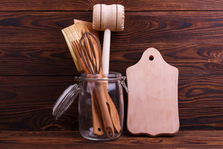 Wooden kitchen tools in a jar with a hammer, spatula, whisk and a wooden fork next to the ditch on a brown backgroundの写真素材