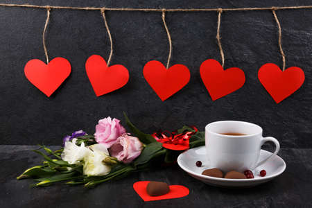 A cup of tea on a stand with a bouquet of Japanese roses and burning candles with hearts on threads...