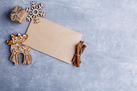 A wooden plaque with different objects in the upper left, cookies in the form of a deer, a snowflake, cinnamon sticks and a gift on a stone backgroundの写真素材