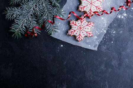 A piece of parchment with a biscuit in the form of snowflakes next to a spruce branch. A red ribbon is powdered on a stone backgroundの写真素材