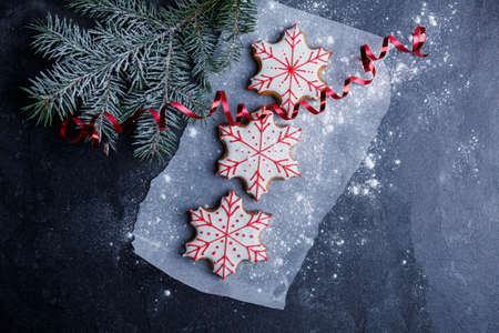 A parchment with biscuits in the form of snowflakes next to a spruce branch and a red ribbon is powdered on a stone background close-up. View from aboveの写真素材