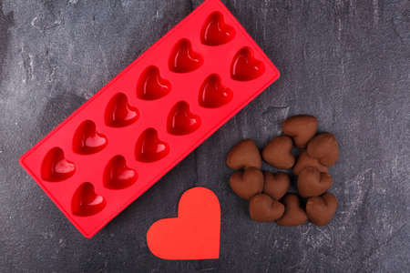 Confectionery silicone red form next to a handful of candies in the form of hearts and a carved heart on a stone background. Top view of a closeupの写真素材