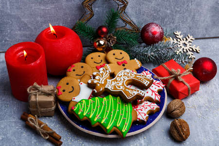 A plate with cookies around red candles and holiday symbols with gifts, nuts, sprigs of fir and toys, cinnamon sticks on a stone backgroundの写真素材