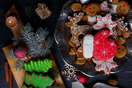 Plate and chipboard with biscuits in the form of fir-trees, little people, snowflakes, deer and gloves on a stone background. Top view of a closeupの写真素材