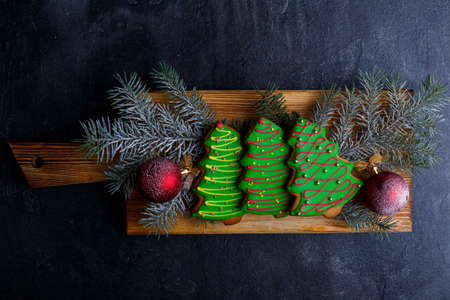 The wooden chipboard lies horizontally with biscuits in the form of Christmas trees with sprigs of spruce and toys on a stone background. View from aboveの写真素材