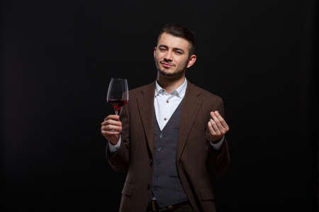 A man with a glass of wine clicks fingers of the other hand on a black backgroundの写真素材
