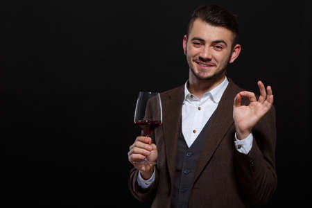 Man with a glass of wine in his hand and gesture that everything is good on a black backgroundの写真素材