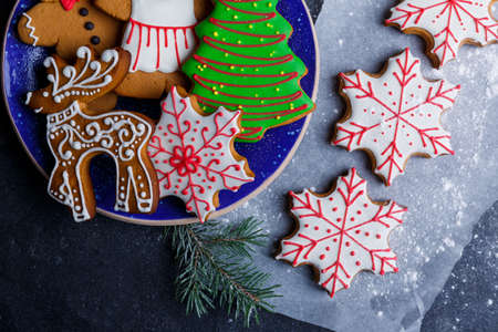 Cookies in a plate in the form of little men, Christmas trees, deer and snowflakes, and on parchment in the form of snowflakes with a branch of a Christmas tree. Top view of a closeupの写真素材