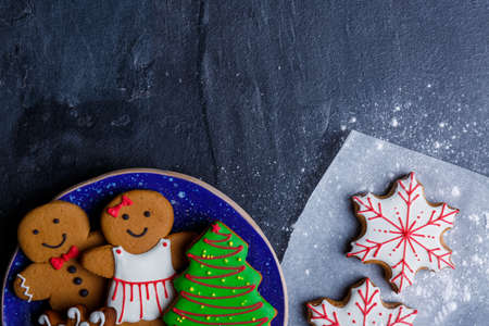 A plate with cookies in the form of little men and a Christmas tree and a biscuit on parchment in a...