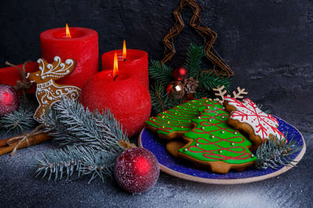 New Year concept with cookies in the form of Christmas trees and snowflakes, red and burning candles and Christmas tree branches and toys is covered with white powder on a stone backgroundの写真素材