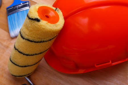Paint roller yellow on an orange hard hat close-up on a wooden backgroundの写真素材