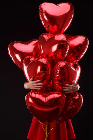 Hands embrace a bunch of air red balloons in the form of hearts on a black backgroundの写真素材