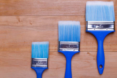 Three different in size blue brushes lie on a ladder. Top view of a wooden backgroundの写真素材