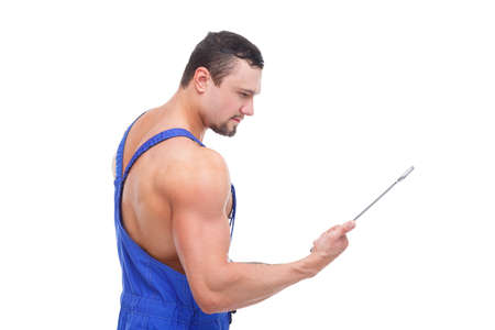 A man is standing sideways looking at a wrench in his hand on a white isolated background